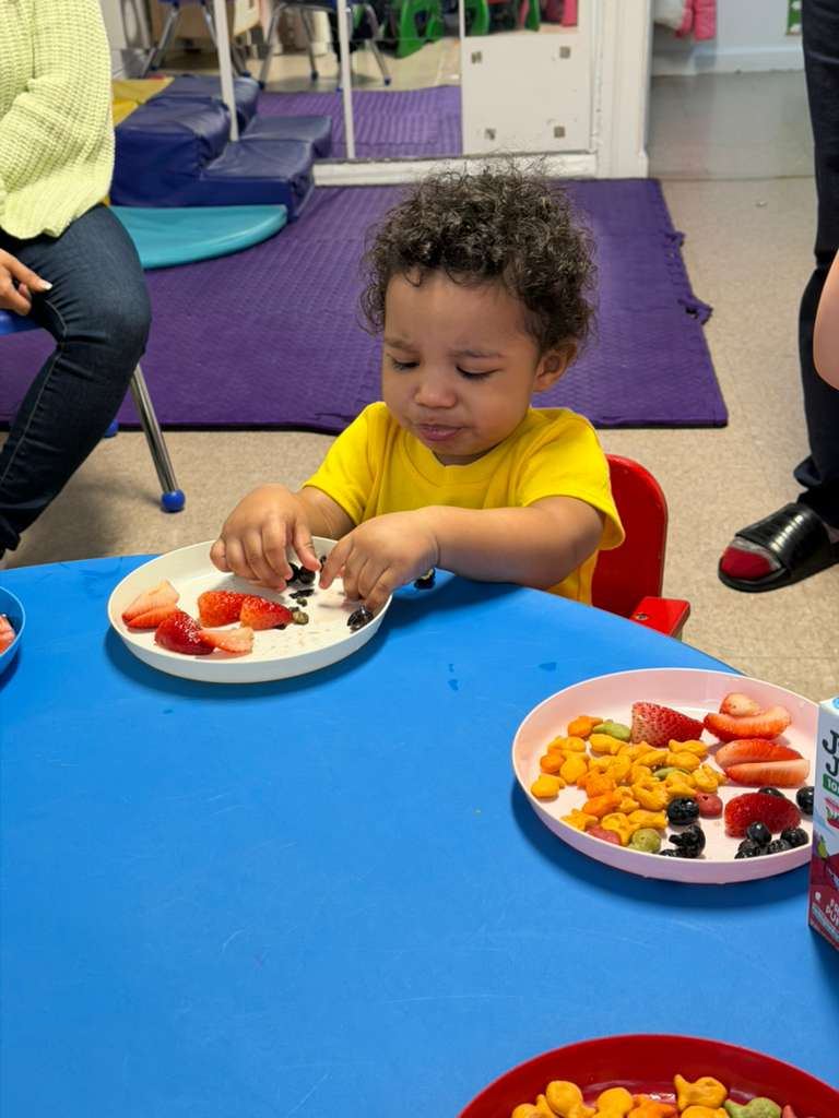 A toddler eating a plate of fresh fruit and vegetables at the table
