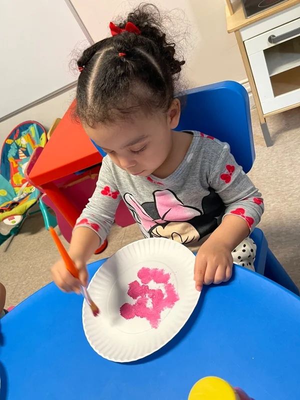 Child painting with a brush on a paper plate at the activity table
