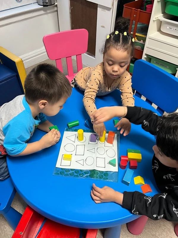 Three children sorting coloured blocks on a shape mat together