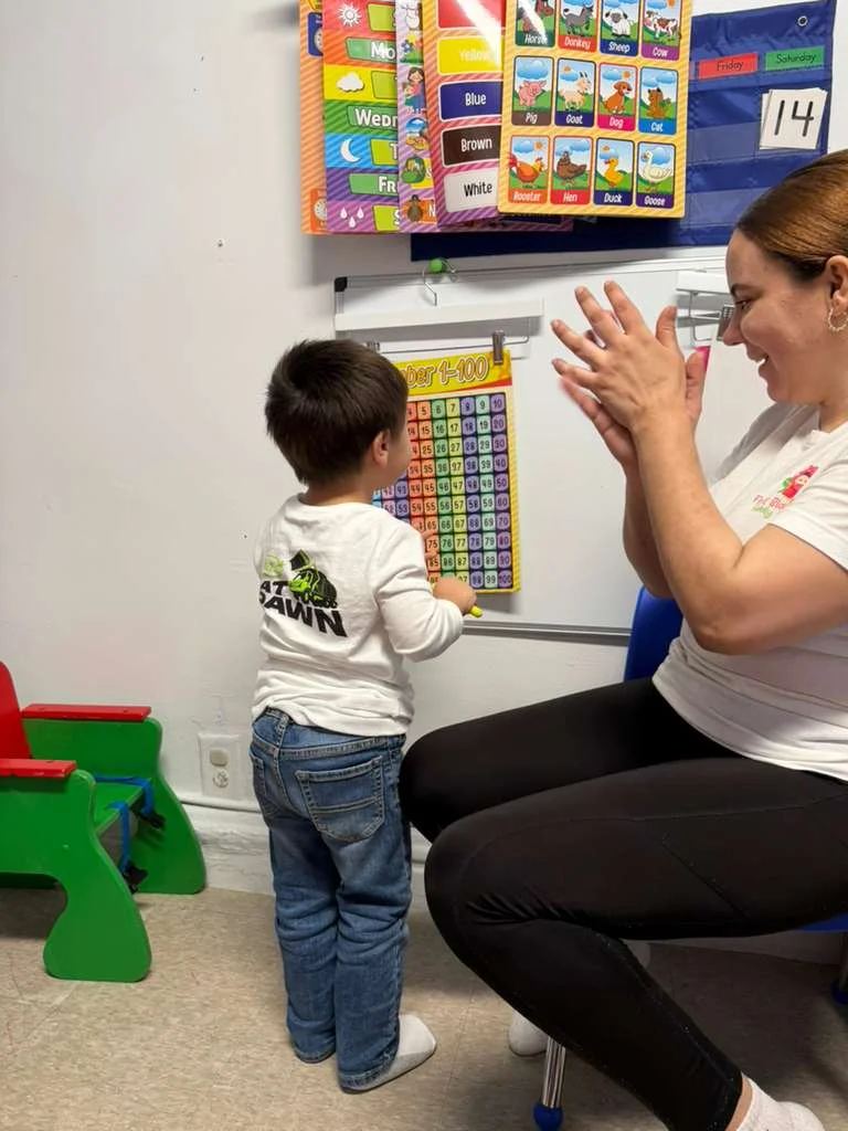 Teacher clapping and encouraging a toddler at the whiteboard