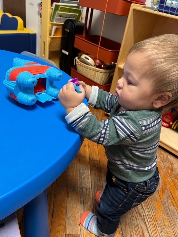 Toddler standing at a low table playing with a toy