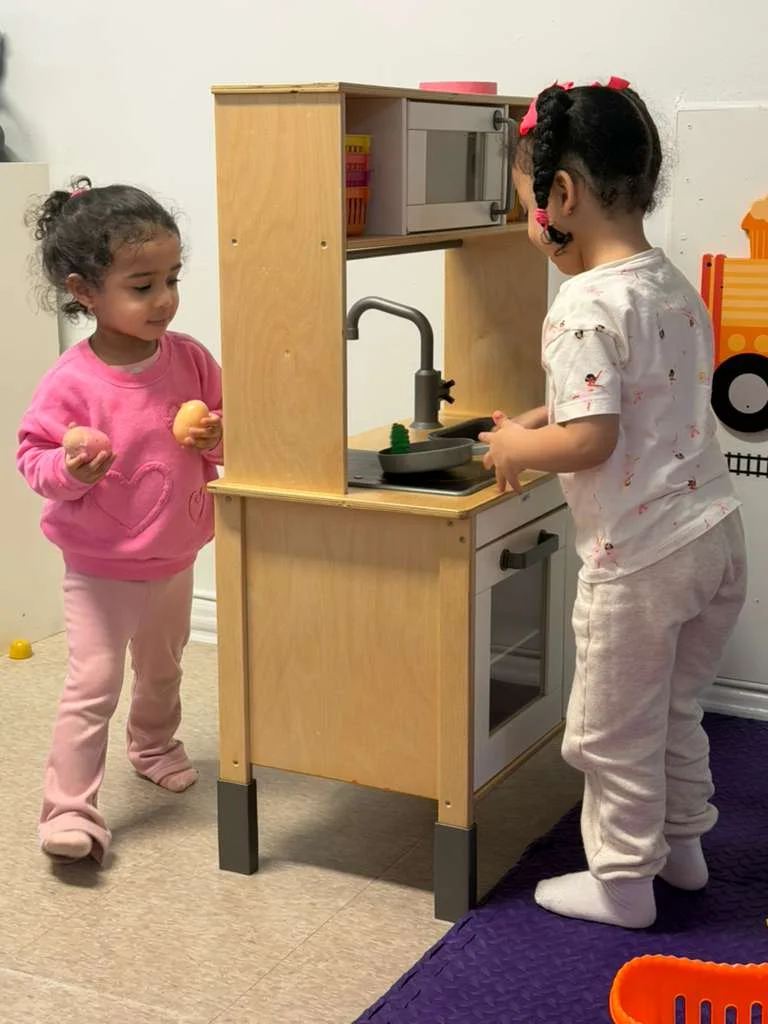 Two toddlers playing together at the wooden play kitchen